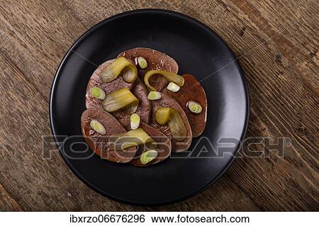 Stock Photograph - Sliced beef tongue with cornichons on black plate. Fotosearch