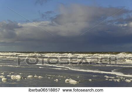 Stock Photo - Waves on a sandy beach, sky with low moving cumulus clouds over the North Sea, Norderney, East Frisian Islands, Lower Saxony, Germany, Europe. Fotosearch