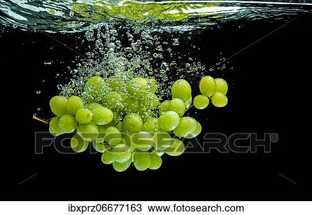 Stock Image - White grapes fall into the water, black background. Fotosearch