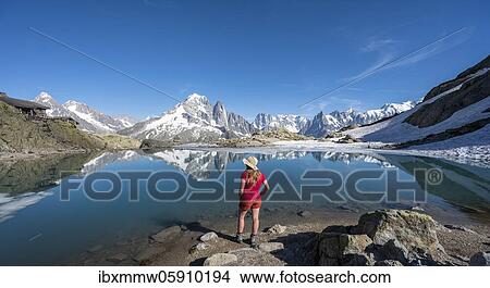 Picture - Young woman in front of mountain panorama, reflection in Lac Blanc, mountain peaks, Grandes Jorasses and Mont Blanc massif, Chamonix-Mont-Blanc, Haute-Savoie, France, Europe. Fotosearch