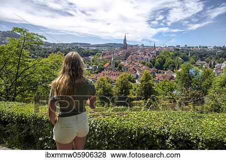 Stock Photo - Young woman looking over the city, city view, view from the rose garden to the old town, Nydegg church and Bernese cathedral, Nydegg district, Bern, Canton of Bern, Switzerland, Europe. Fotosearch
