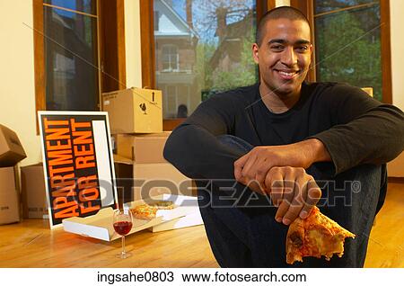 Stock Image - Man having pizza and red wine in empty apartment. Fotosearch