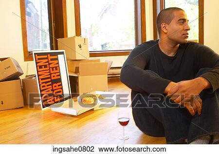 Stock Image - Man sitting in empty apartment with glass of wine. Fotosearch