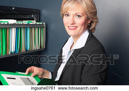 Stock Image - Smiling businesswoman reading file 1. Fotosearch
