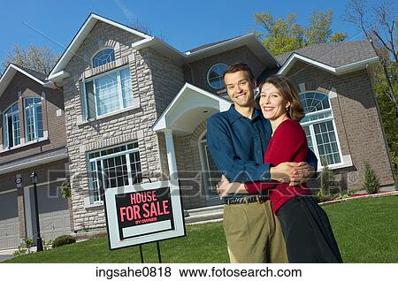 Stock Photo - Smiling young couple in front of their new home. Fotosearch