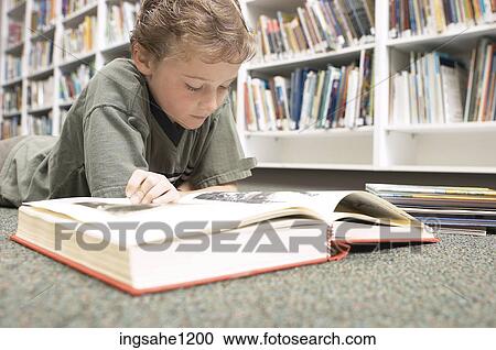 Stock Image - Little boy reading book in library. Fotosearch
