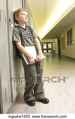 Stock Image - Little boy with school books leaning against lockers 4. Fotosearch