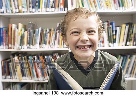 Smiling little boy holding book in library View Large Photo Image Stock Photo - Smiling little boy holding book in library. Fotosearch