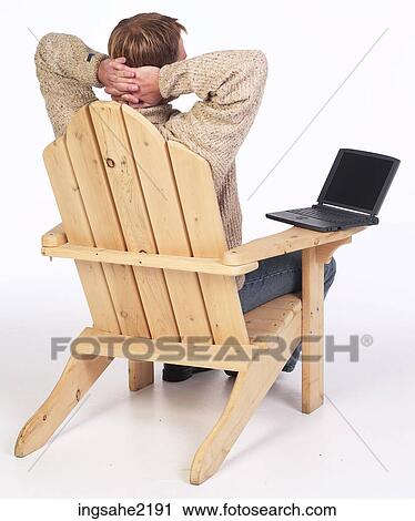 Stock Image - Man in wooden chair working on laptop computer . Fotosearch