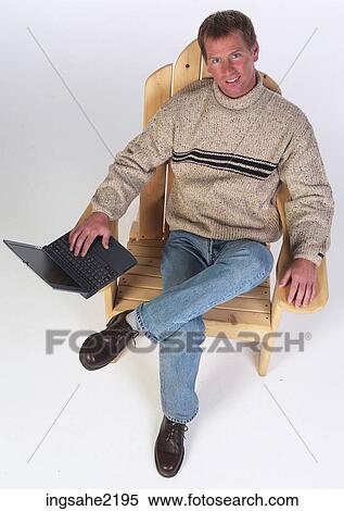 Man in wooden chair working on laptop computer View Large Photo Image Stock Photography - Man in wooden chair working on laptop computer . Fotosearch