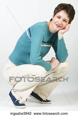 Stock Image - Crouching woman in casual attire smiling . Fotosearch