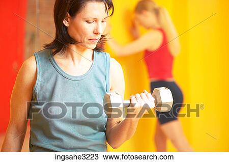 Mature adult woman lifting weights with woman stretching in background View Large Photo Image Stock Image - Mature adult woman lifting weights with woman stretching in background . Fotosearch