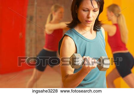 Mature adult woman lifting weights with woman stretching in background View Large Photo Image Stock Photo - Mature adult woman lifting weights with woman stretching in background . Fotosearch