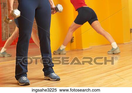 Mature adult woman lifting weights with woman stretching in background View Large Photo Image Stock Photography - Mature adult woman lifting weights with woman stretching in background . Fotosearch