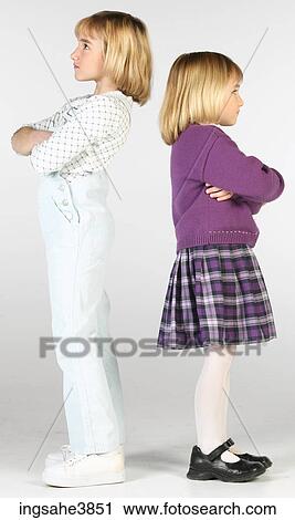 Stock Image - Two Caucasian blonde girls standing with their backs towards each other. Fotosearch