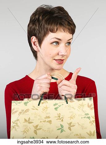 Picture - Young woman clutching shopping bags and pointing towards an object. Fotosearch