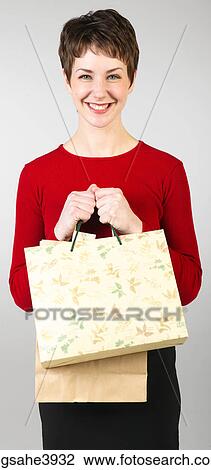 Stock Image - Young woman clutching shopping bags and smiling. Fotosearch