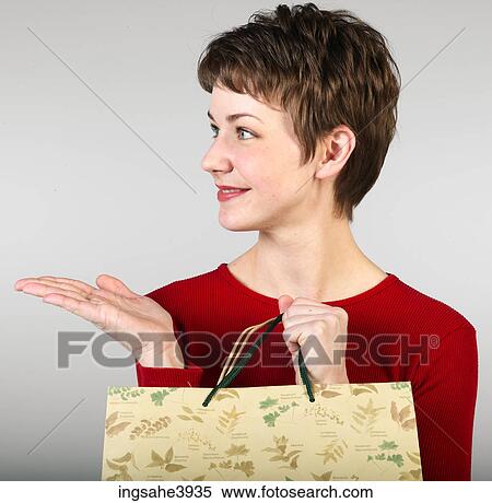 Young woman clutching shopping bags and pointing towards an object View Large Photo Image Stock Photography - Young woman clutching shopping bags and pointing towards an object . Fotosearch
