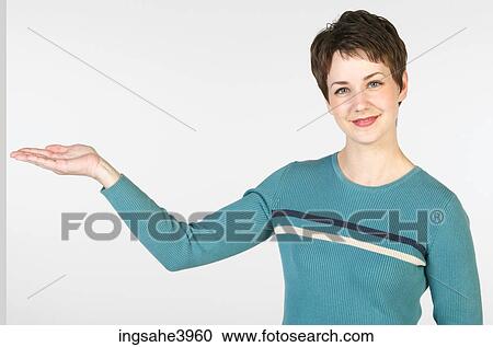 Stock Image - Young woman standing and pointing towards an object. Fotosearch