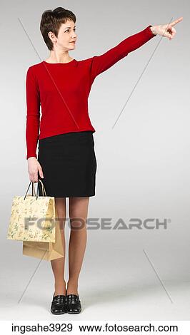 Stock Photo - Young woman standing with shopping bags and pointing towards an object . Fotosearch