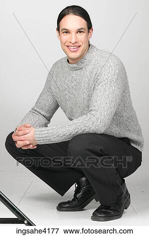 Stock Photo - Man in gray sweater smiling and crouching on the floor. Fotosearch