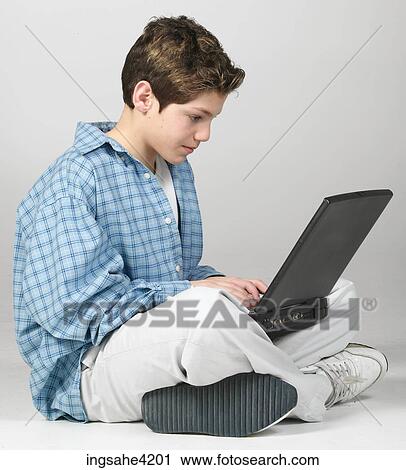 Stock Image - Seated teenaged boy using laptop computer. Fotosearch