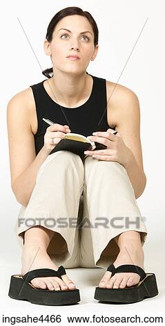 Stock Photograph - Seated young woman thinking and writing in book. Fotosearch