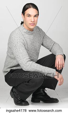 Serious man in gray sweater crouching on the floor View Large Photo Image Stock Photo - Serious man in gray sweater crouching on the floor . Fotosearch
