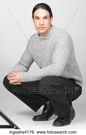 Serious man in gray sweater crouching on the floor View Large Photo Image Stock Photograph - Serious man in gray sweater crouching on the floor . Fotosearch