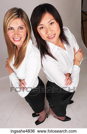 Two young business women standing back to back View Large Photo Image Stock Photograph - Two young business women standing back to back. Fotosearch