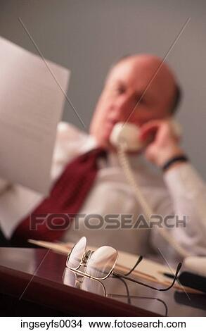 Man on Phone in Office Holding Document View Large Photo Image Picture - Man on Phone in Office Holding Document. Fotosearch