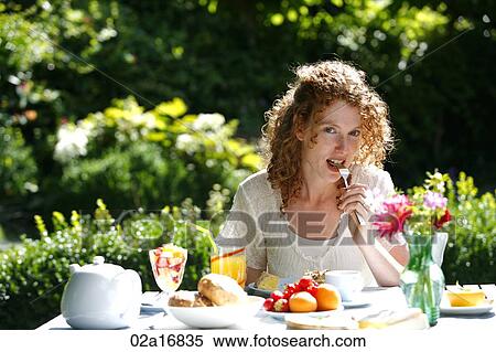 Stock Photography - A beautiful woman eating a meal in her garden. Fotosearch