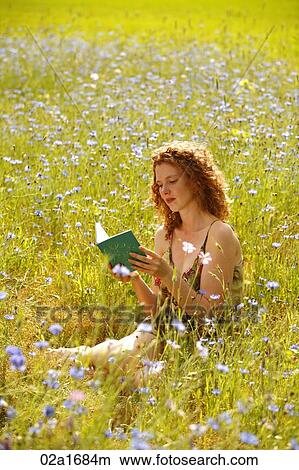 Picture - A beautiful woman reading a book in a field of flowers. Fotosearch