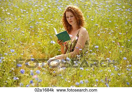 Stock Image - A beautiful woman reading a book in a field of flowers. Fotosearch