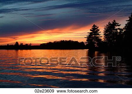 Stock Photo - Beautiful orange sunset over lake front.. Fotosearch