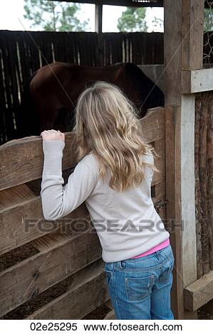 Stock Photography - Blond girl looking over stable wall at Mountain Pine Ridge Reserve. Fotosearch