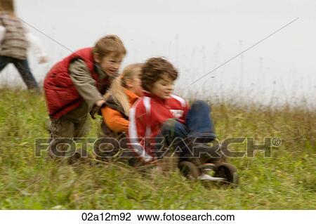 Boy and girl riding a mountain board with a boy pushing them from behind View Large Photo Image Stock Image - Boy and girl riding a mountain board with a boy pushing them from behind. Fotosearch