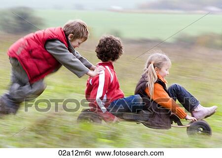 Stock Photograph - Boy and girl riding a mountain board with a boy pushing them from behind. Fotosearch