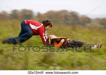 Stock Image - Boy pushing a mountain board and a girl lying on it. Fotosearch