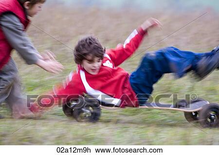Stock Image - Boy riding a mountain board with another boy pushing him from behind. Fotosearch