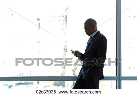 Businessman silhouetted in large office window, using PDA smart phone. View Large Photo Image Stock Photography - Businessman silhouetted in large office window, using PDA smart phone.. Fotosearch