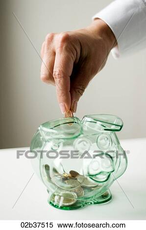 Stock Photography - Close-up of hand dropping a coin into a piggy bank. Fotosearch