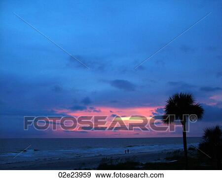 Stock Photo - Couple walking in the distance on tropical beach during sunset.. Fotosearch