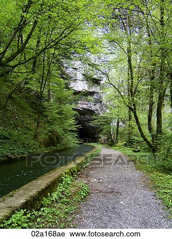 Stock Image - Dirt path leading to a cave. Fotosearch