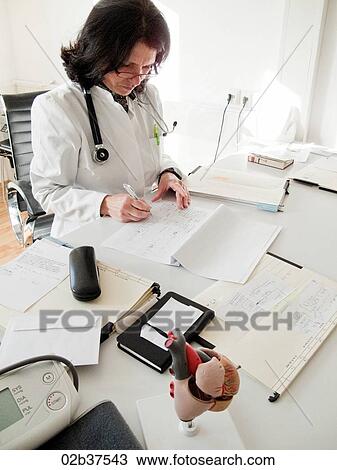 Stock Image - Doctor reading patients files at her desk. Fotosearch