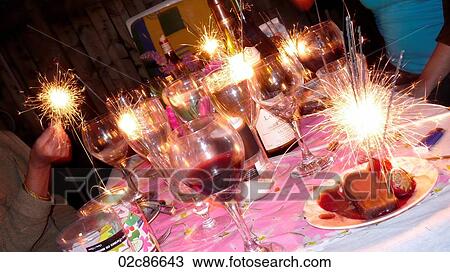 Stock Image - Friends celebrating at table with sparklers.. Fotosearch