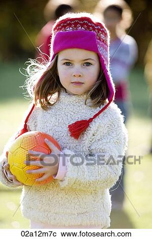 Stock Image - Girl holding a ball standing in a park. Fotosearch