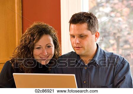Stock Image - Husband and wife working on home wireless laptop computer.. Fotosearch