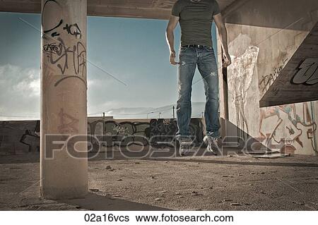 Stock Photograph - Low section of a man jumping in vandalised car lot. Fotosearch