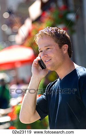 Stock Photo - Man talking on PDA cell phone in front of street cafe.. Fotosearch